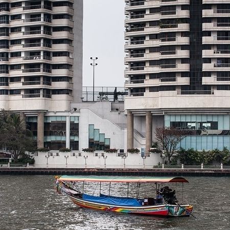 Ein buntes, kleines Boot schwimmt auf einem Fluss vor zwei großen Hochhäusern