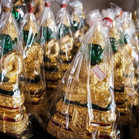 Kleine Figuren einer religiösen Figur in Gold, rot und grün sind in Folie eingepackt und mit Preisen versehen