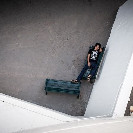Aus einer erhöhten Position ist zu sehen, wie an Mann auf einer Bank an einer weißen Mauer liegt