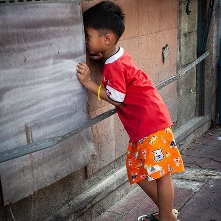 Ein kleiner Junge späht durch einen Schlitz in einer Wand hindurch