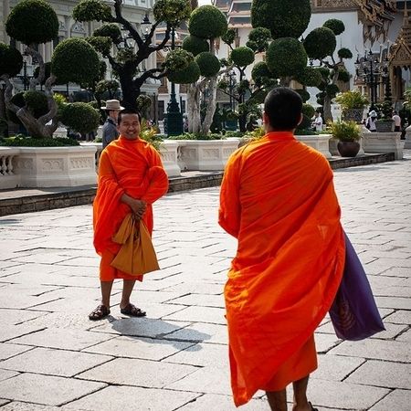 Zwei Männer in langen, orangen Gewändern stehen sich gegenüber, hinter ihnen sind reich verzierte Häuser und frisch beschnittene kleine Bäume zu sehen