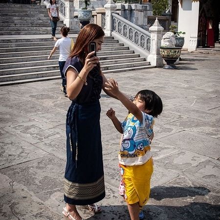 Eine Frau hält ein Handy in der Hand, ein kleiner Junge streckt seinen Arm danach aus