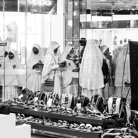 Frauen mit langen weißen Gewändern und Kopftüchern sind in einem Einkaufszentrum, das Bild ist schwarz weiß