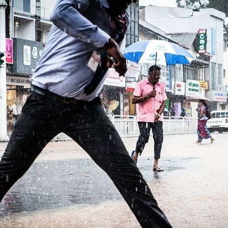Im Regen überqueren Personen eine Straße, manche haben einen Regenschirm bei sich