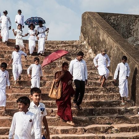 Viele Leute gehen eine Steintreppe hinab, alle tragen Weiß außer einem Mann mit rotem Gewand und rotem Schirm