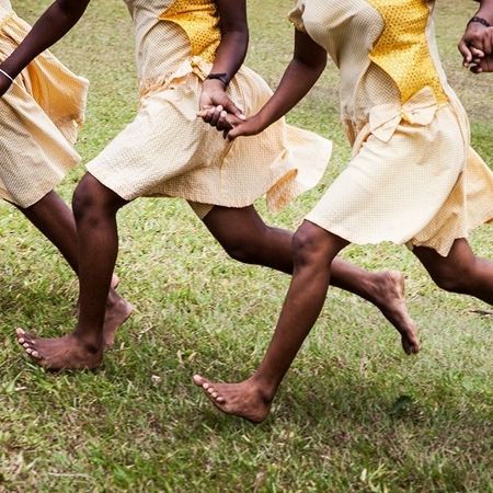 Füße von Personen in gelb weißen Kleidern, die Hand haltend über eine Wiese laufen