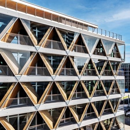 Drohnenaufnahme von einer geometrischen Fassade eines modernen Gebäudes mit einem Muster aus dreieckigen Holzpaneelen und Glas
