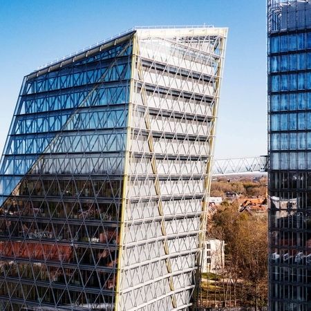 Drohnenaufnahme von einem modernen Hochhaus mit diagonaler Gitterfassade vor klarem blauen Himmel