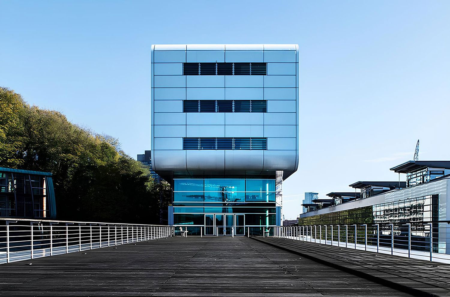 Ein modernes Gebäude in Kubus-Form, die Ecken sind abgerundet und die Wände des Sockel-Bereichs sind aus Glas
