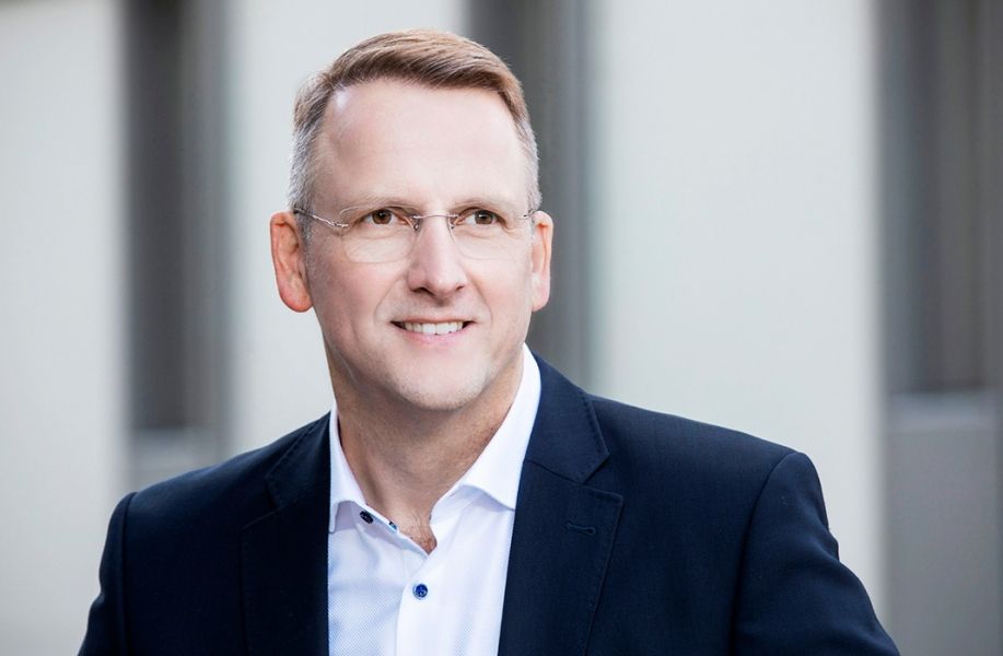 Ein Mann mit Brille und kurzen Haaren in einem Anzug lächelt freundlich